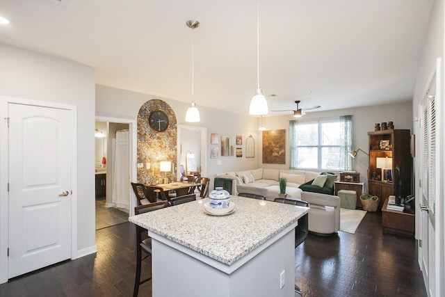 kitchen featuring ceiling fan, a center island, hanging light fixtures, dark hardwood / wood-style floors, and a kitchen bar