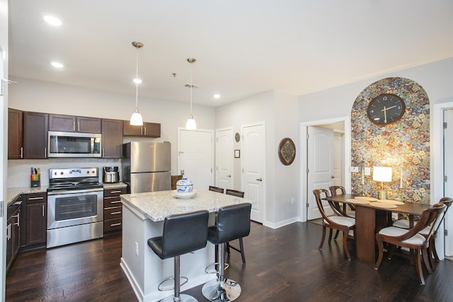 kitchen with light stone countertops, appliances with stainless steel finishes, decorative light fixtures, a kitchen island, and a kitchen bar