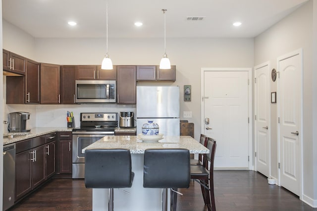 kitchen with a kitchen bar, appliances with stainless steel finishes, tasteful backsplash, dark brown cabinets, and decorative light fixtures