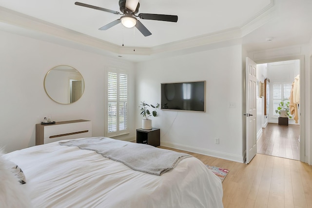 bedroom with light wood-type flooring, a tray ceiling, ceiling fan, and ornamental molding