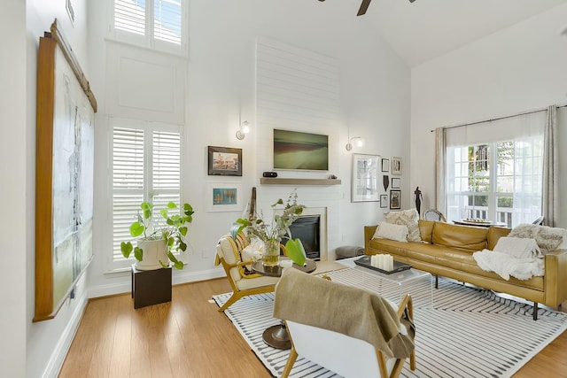 living room with ceiling fan, a fireplace, high vaulted ceiling, and light wood-type flooring