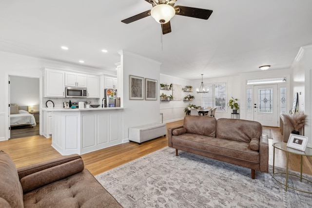 living room with ceiling fan with notable chandelier, ornamental molding, and light hardwood / wood-style floors