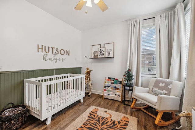 bedroom with a nursery area, dark hardwood / wood-style floors, and ceiling fan