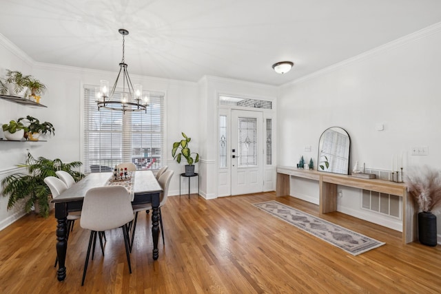 dining area with wood-type flooring, ornamental molding, and a notable chandelier