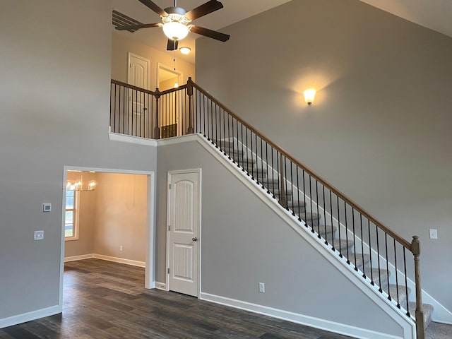 staircase with hardwood / wood-style floors, ceiling fan with notable chandelier, and a high ceiling