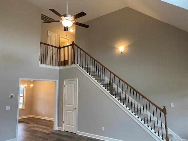 stairs with ceiling fan with notable chandelier, hardwood / wood-style flooring, and high vaulted ceiling