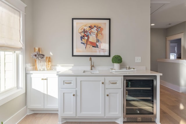 bar with white cabinets, sink, wine cooler, and light hardwood / wood-style floors