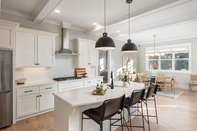 kitchen featuring white cabinetry, an island with sink, stainless steel fridge, beam ceiling, and wall chimney exhaust hood