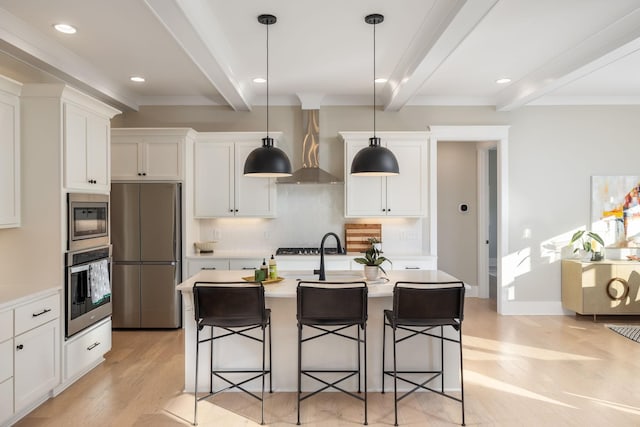 kitchen with a kitchen island with sink, beamed ceiling, wall chimney exhaust hood, and appliances with stainless steel finishes