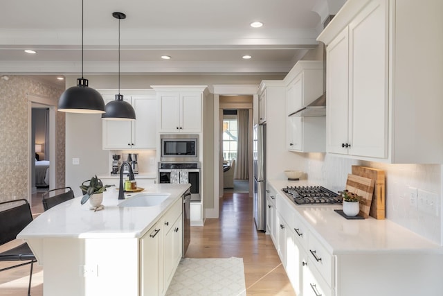 kitchen featuring sink, white cabinets, hanging light fixtures, stainless steel appliances, and a center island with sink