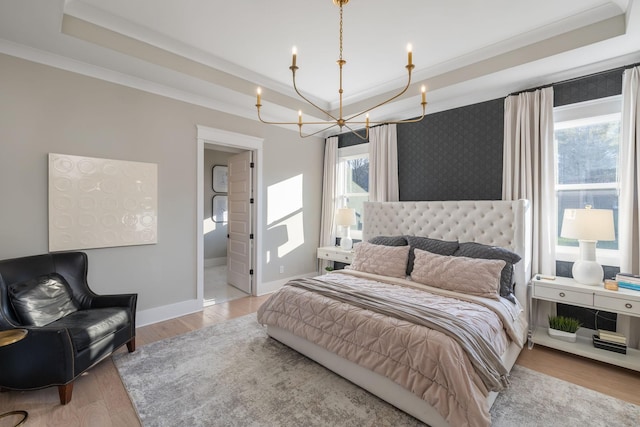 bedroom with a chandelier, light hardwood / wood-style floors, a raised ceiling, crown molding, and ensuite bath