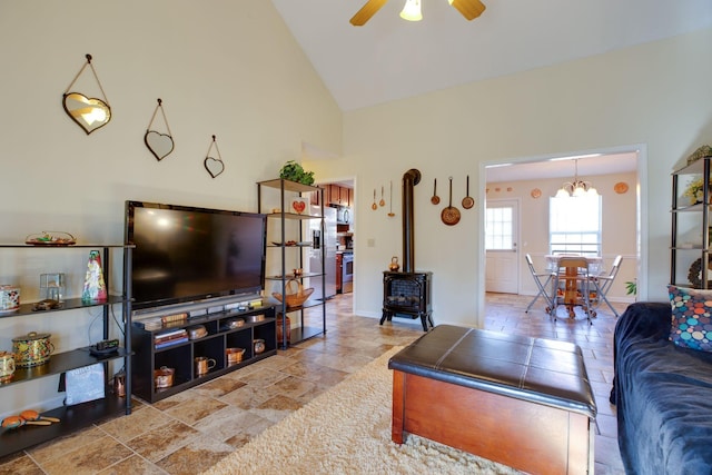 living room featuring ceiling fan with notable chandelier, high vaulted ceiling, and a wood stove