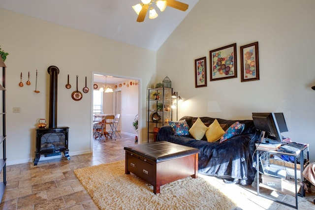 living room featuring ceiling fan with notable chandelier, high vaulted ceiling, and a wood stove