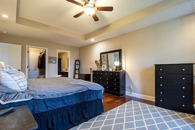 bedroom with dark wood-type flooring, a walk in closet, ceiling fan, a tray ceiling, and a closet