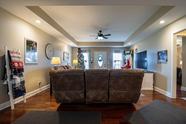 living room featuring ceiling fan, dark hardwood / wood-style flooring, and a tray ceiling