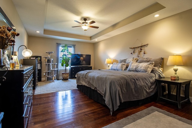 bedroom featuring dark hardwood / wood-style flooring, a tray ceiling, and ceiling fan