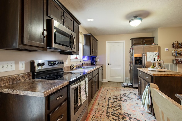 kitchen featuring sink, light tile patterned floors, a textured ceiling, dark brown cabinetry, and stainless steel appliances