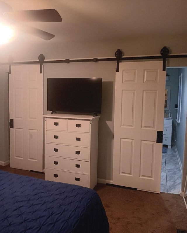 unfurnished bedroom featuring a barn door, ceiling fan, and dark colored carpet