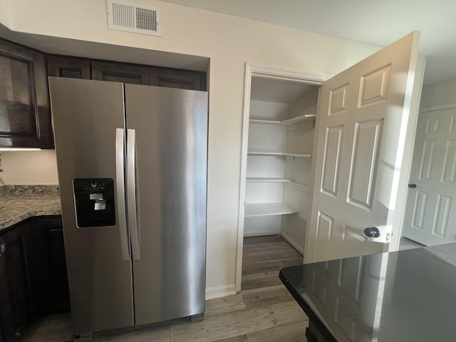 kitchen with light hardwood / wood-style floors, dark brown cabinetry, stainless steel fridge with ice dispenser, and stone counters