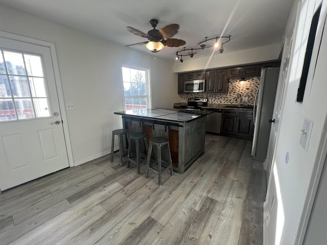 kitchen with sink, decorative backsplash, ceiling fan, appliances with stainless steel finishes, and a kitchen bar