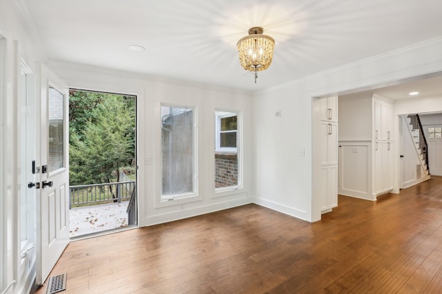 spare room with wood-type flooring, crown molding, and a notable chandelier