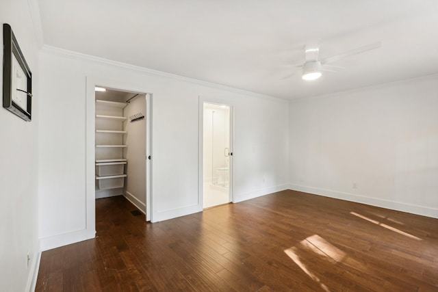 unfurnished bedroom with dark wood-type flooring, crown molding, ceiling fan, a spacious closet, and a closet