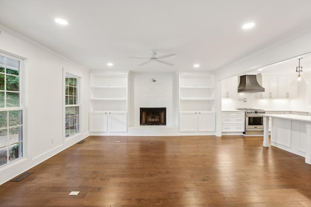 unfurnished living room with ceiling fan, dark hardwood / wood-style flooring, ornamental molding, and a brick fireplace