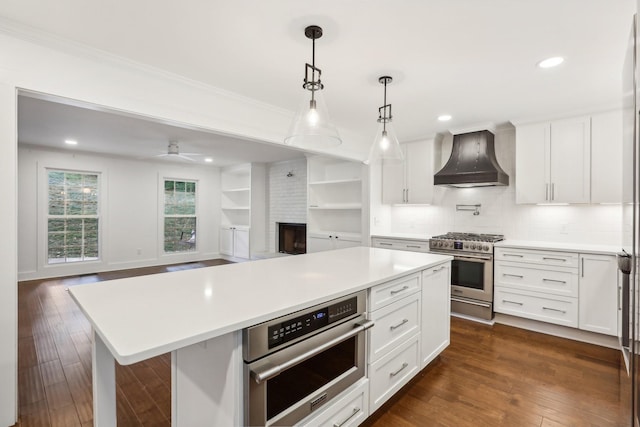 kitchen featuring white cabinetry, a center island, hanging light fixtures, stainless steel appliances, and premium range hood