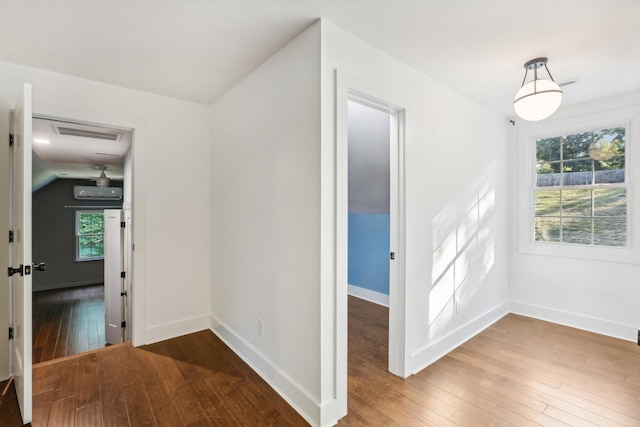 hallway featuring a wall mounted air conditioner, wood-type flooring, and plenty of natural light