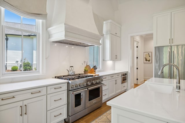 kitchen with light wood-type flooring, premium range hood, high end appliances, sink, and white cabinets