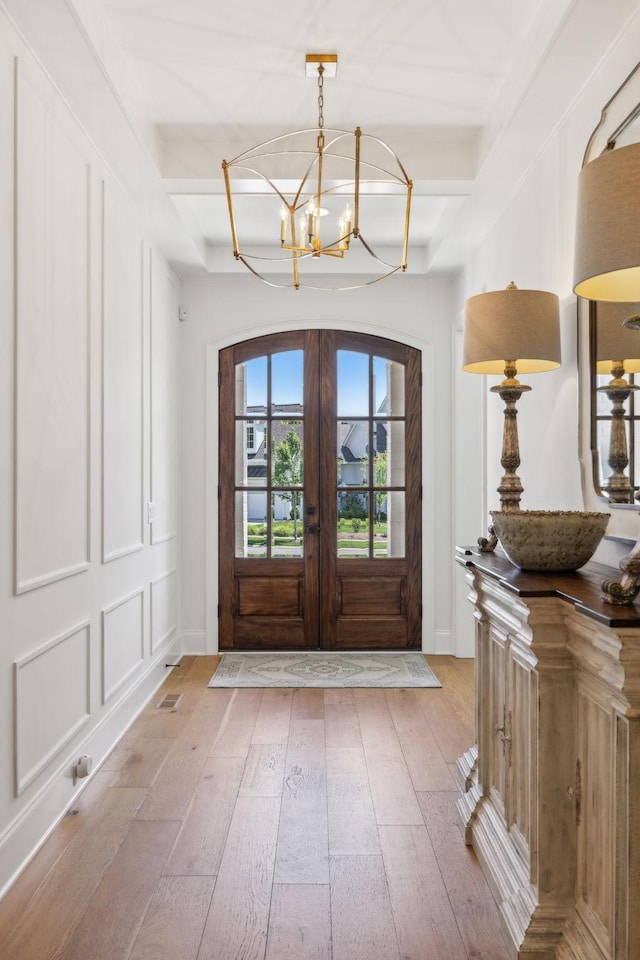 entrance foyer featuring french doors, beamed ceiling, hardwood / wood-style floors, and an inviting chandelier