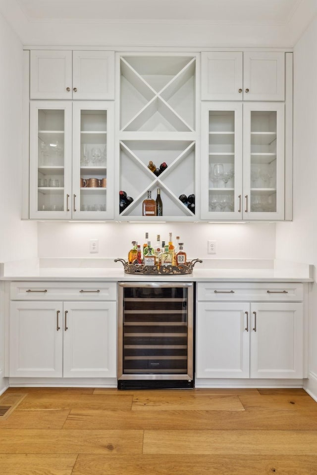 bar with wine cooler, white cabinetry, and light hardwood / wood-style flooring