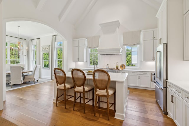 kitchen featuring high quality fridge, a center island, light hardwood / wood-style flooring, vaulted ceiling with beams, and white cabinetry