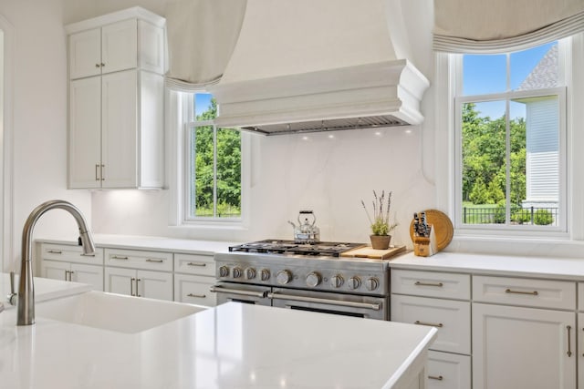 kitchen featuring white cabinets, a healthy amount of sunlight, high end stove, and custom range hood