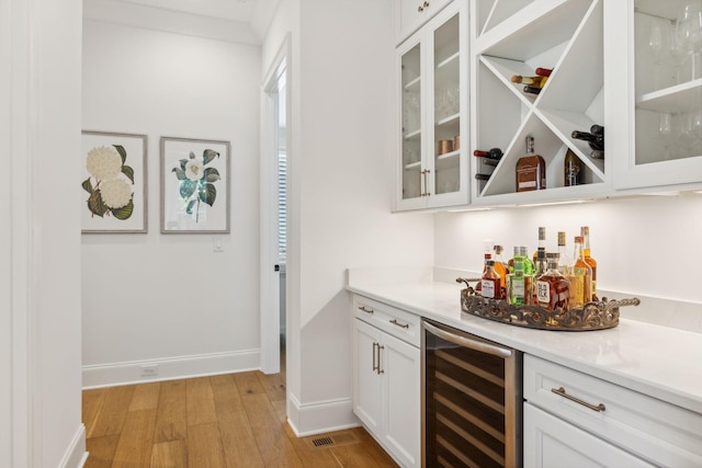 bar with light hardwood / wood-style floors, light stone counters, white cabinetry, and beverage cooler