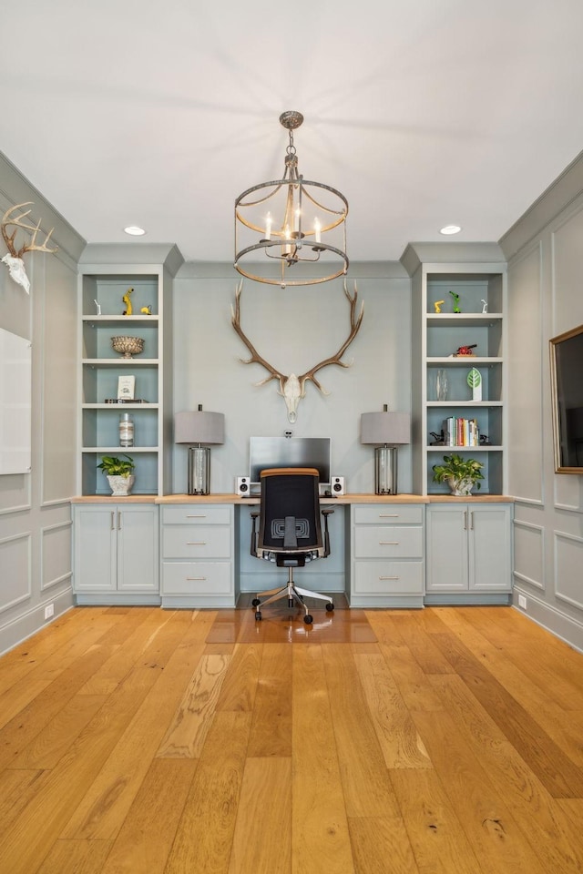 unfurnished office featuring built in features, light wood-type flooring, built in desk, and a chandelier