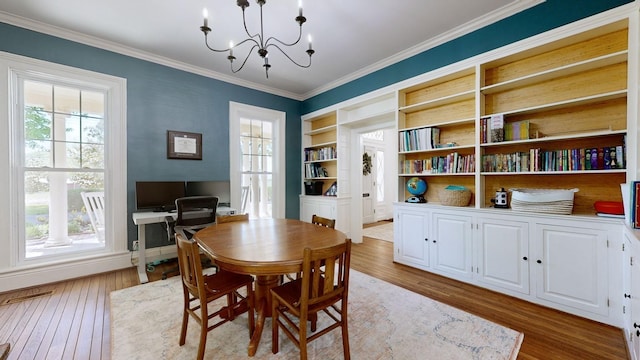 dining area featuring built in shelves, light hardwood / wood-style floors, ornamental molding, and a chandelier