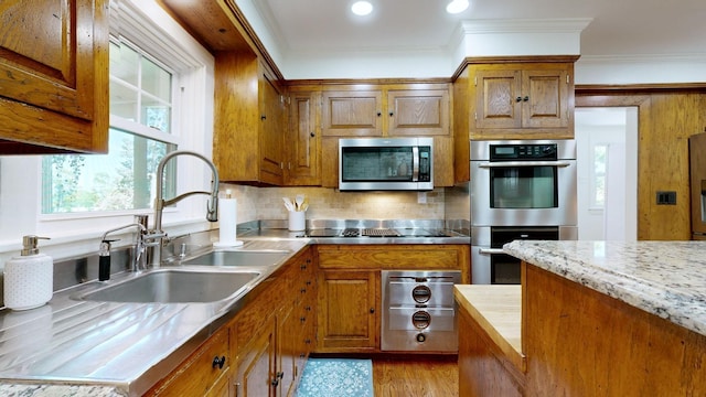 kitchen with appliances with stainless steel finishes, tasteful backsplash, ornamental molding, sink, and light hardwood / wood-style flooring