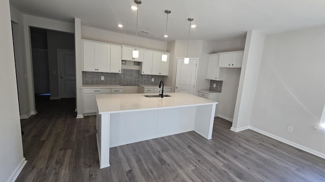 kitchen with decorative backsplash, a sink, a kitchen island with sink, and white cabinetry