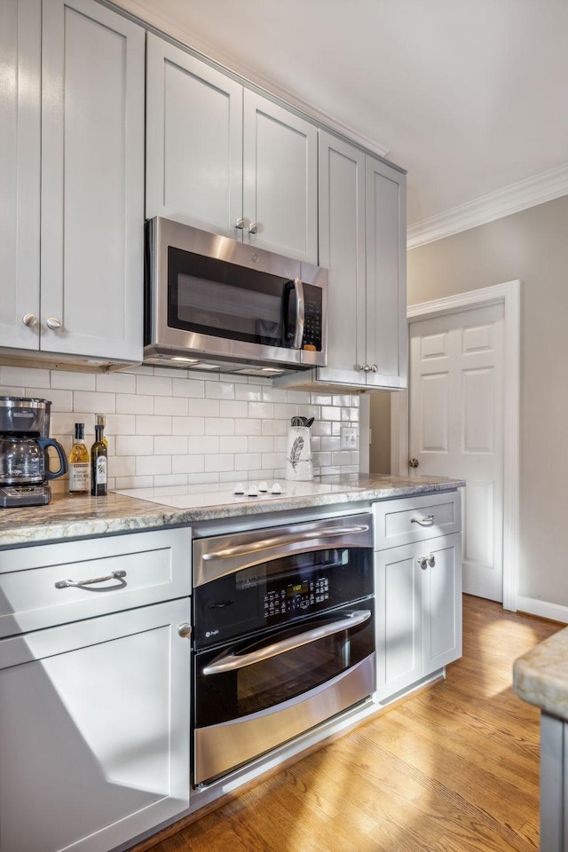 kitchen with light stone countertops, appliances with stainless steel finishes, backsplash, light wood-type flooring, and ornamental molding