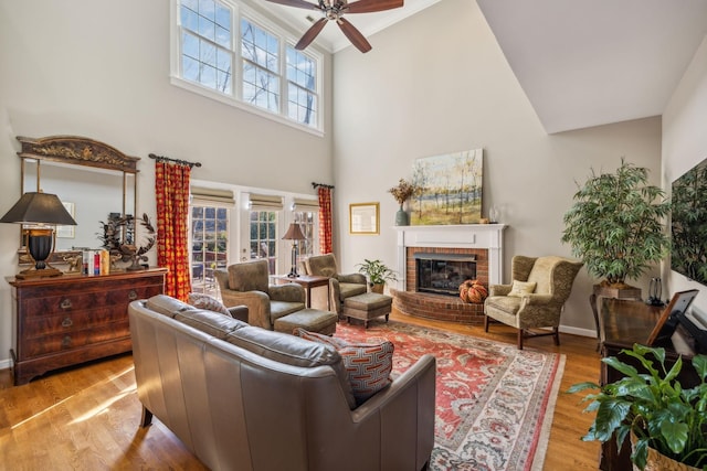 living room featuring french doors, ceiling fan, a fireplace, a high ceiling, and light hardwood / wood-style floors