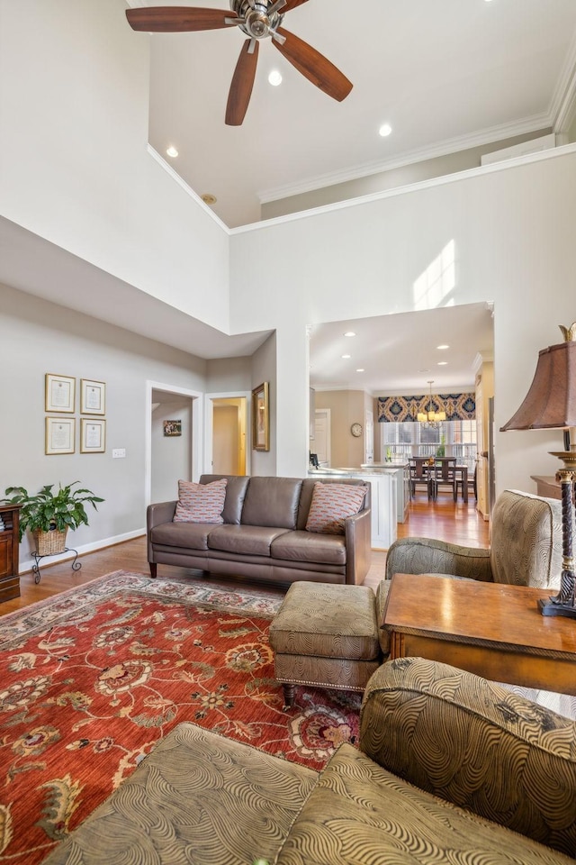 living room with ceiling fan, a towering ceiling, light wood-type flooring, and ornamental molding