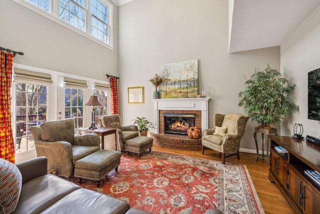 living room featuring wood-type flooring, a high ceiling, and a brick fireplace