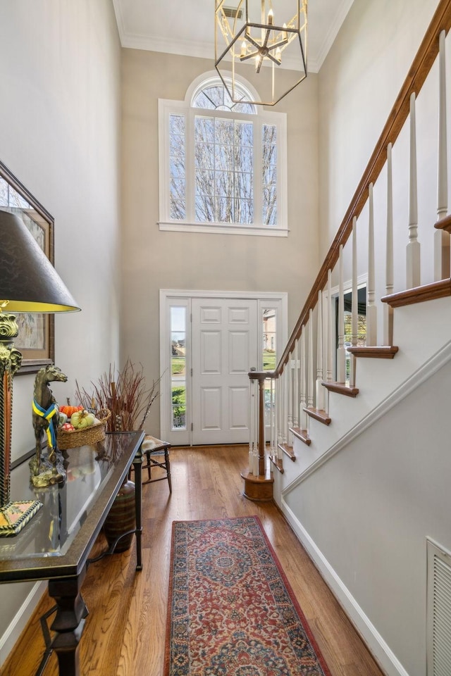 foyer featuring hardwood / wood-style flooring, ornamental molding, a high ceiling, and an inviting chandelier