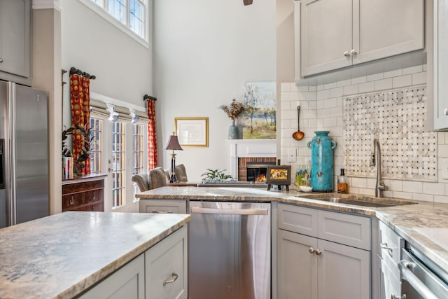 kitchen with light stone countertops, sink, stainless steel appliances, a brick fireplace, and decorative backsplash