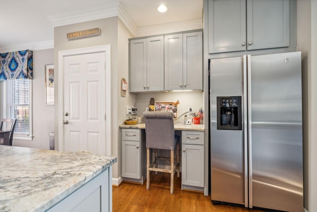 kitchen with gray cabinetry, crown molding, stainless steel refrigerator with ice dispenser, light stone countertops, and light hardwood / wood-style floors