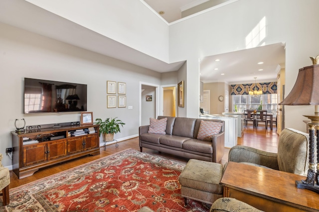 living room with a chandelier, a towering ceiling, hardwood / wood-style flooring, and ornamental molding