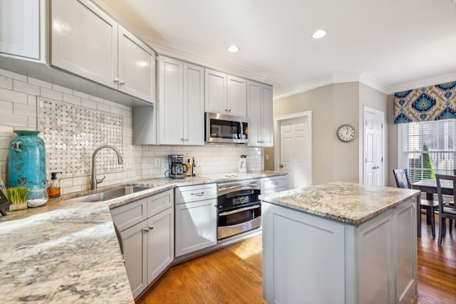 kitchen featuring appliances with stainless steel finishes, tasteful backsplash, light stone counters, sink, and light hardwood / wood-style flooring