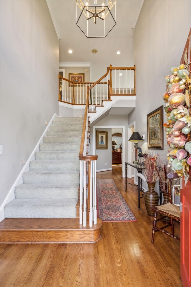 stairway with a chandelier, hardwood / wood-style floors, a towering ceiling, and ornamental molding