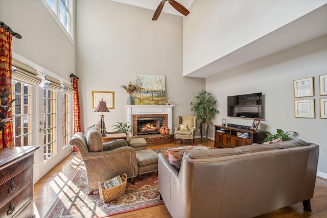 living room featuring wood-type flooring, a towering ceiling, a brick fireplace, and ceiling fan